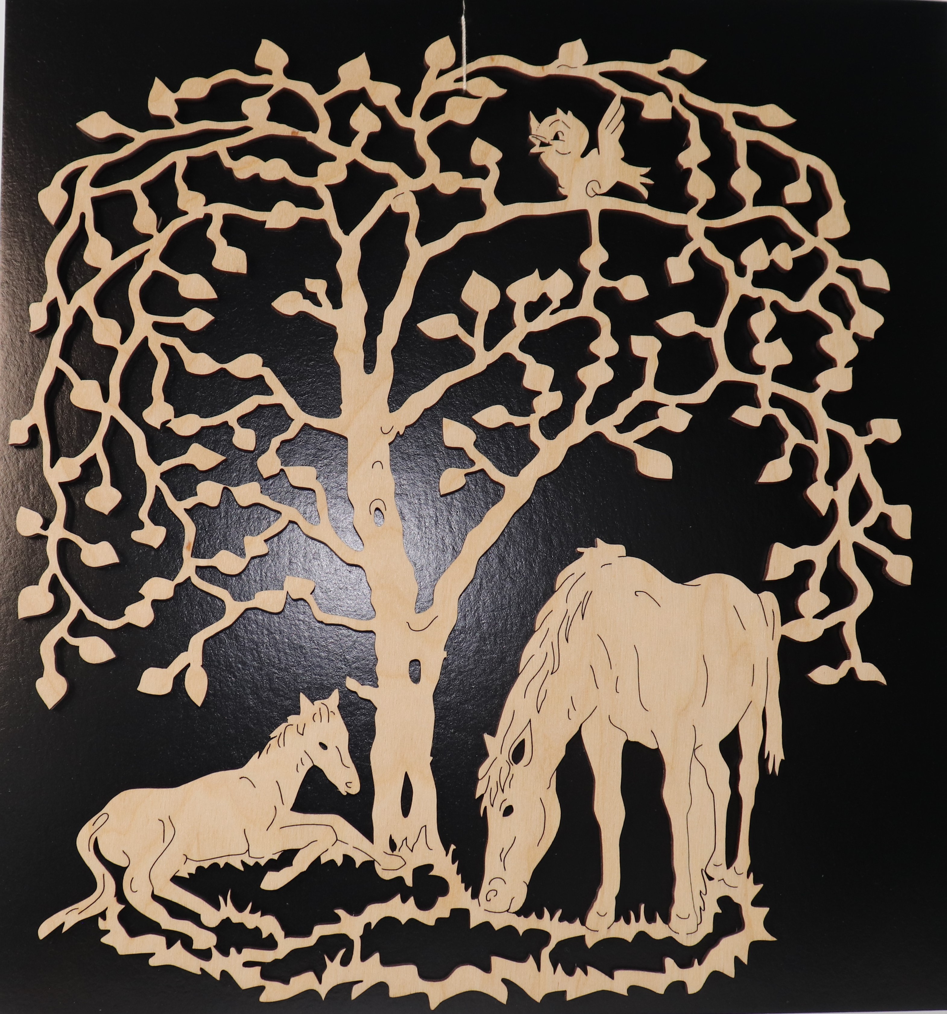 Fensterbild aus Holz mit Pferden unter Bäumen als Motiv.