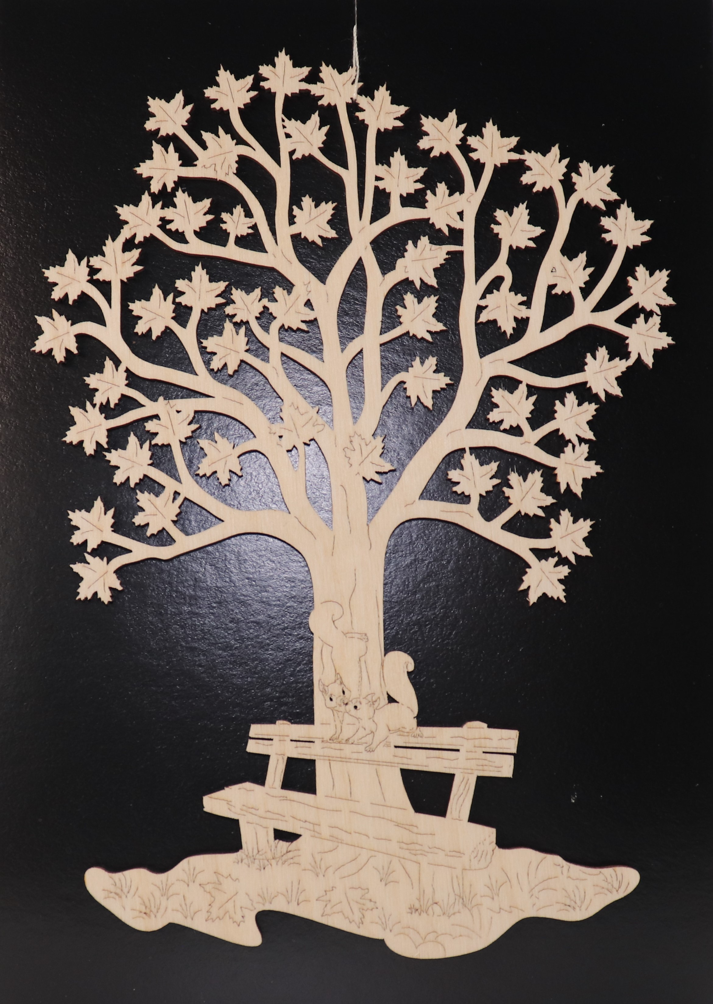 Fensterbild aus Holz mit Motiv "Baum mit Bank und Eichhörnchen".