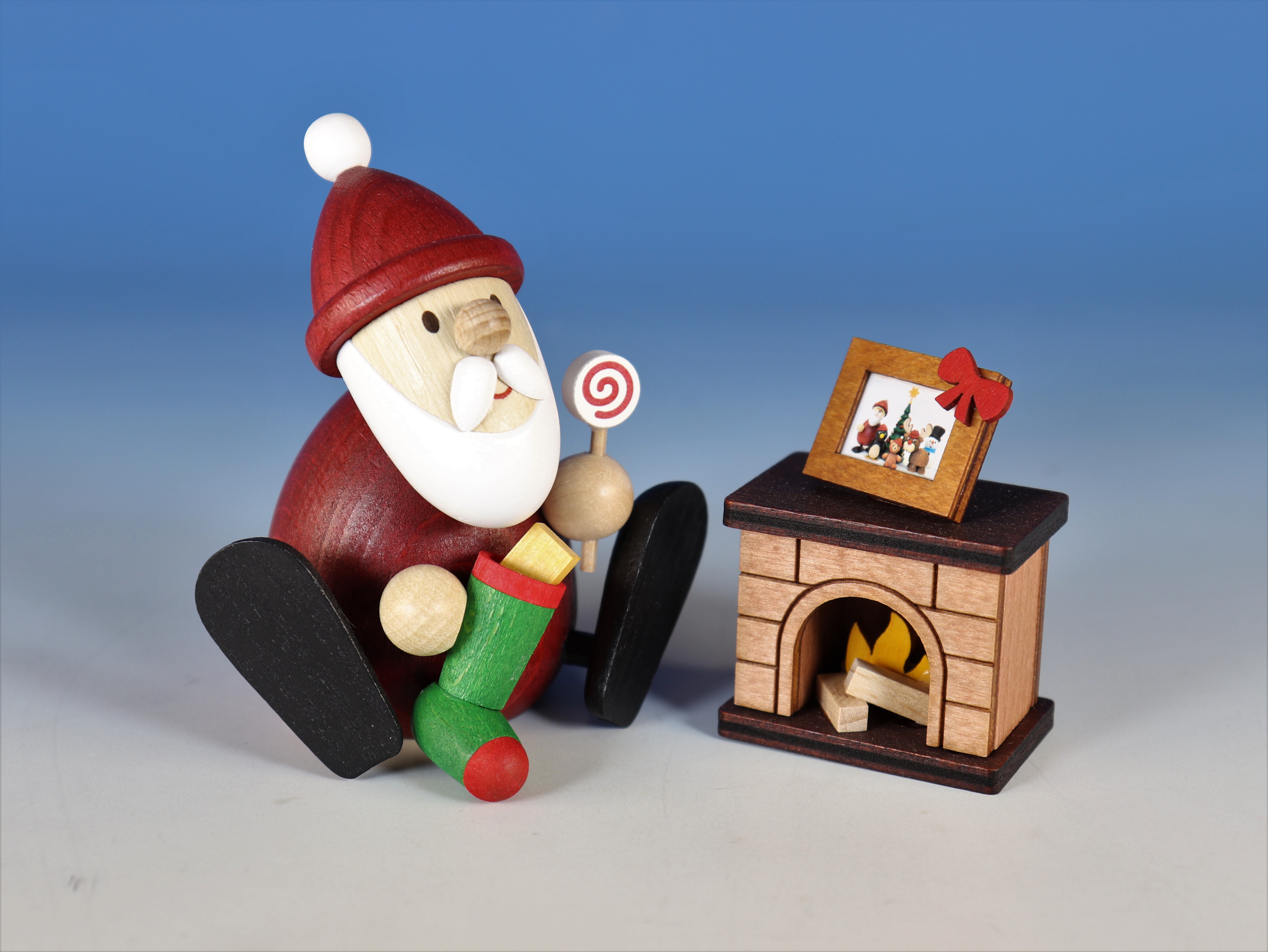 Detailreich gestaltete und bunt bemalte Holzifguren Weihnachtsmann und Kamin  vor blauem Hintergrund.