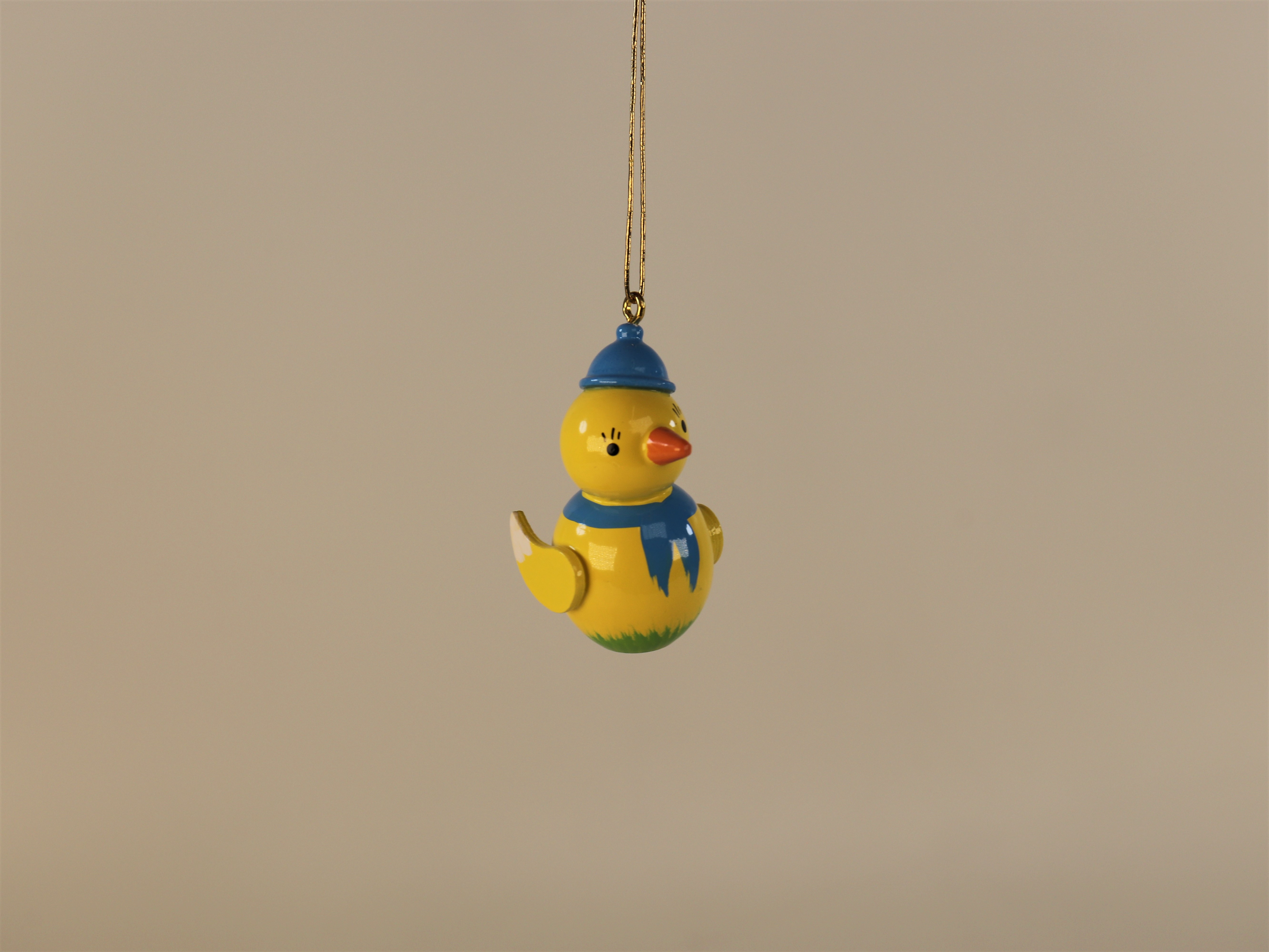 Oster-Tischdeko Küken mit blauer Mütze und Schal auf grünem Sockel