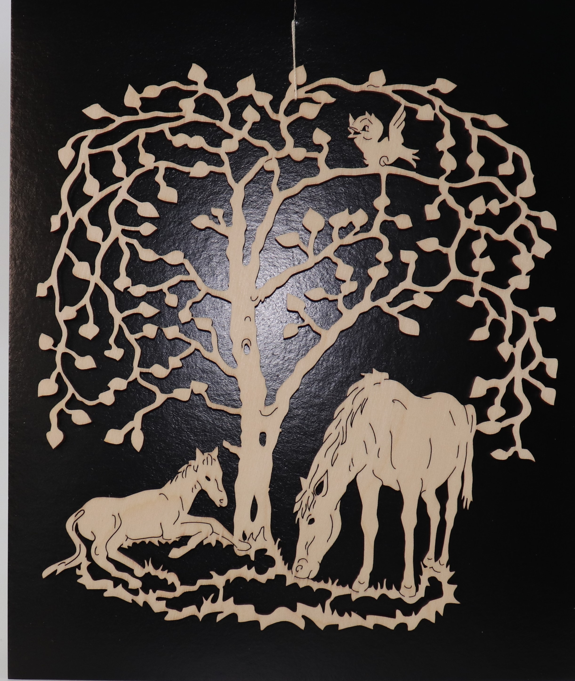 Fensterbild aus Holz mit einem Baum und zwei Pferden darunter als Motiv.